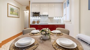 Un comedor con una mesa redonda dispuesta para cuatro, una cocina al fondo y un reloj en la pared.