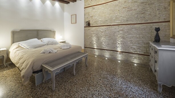 Ein Schlafzimmer mit Bett, Bank, Kommode und einer Steinwand.