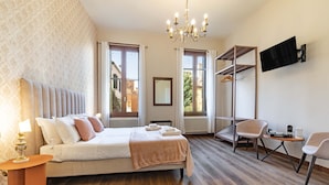 Una habitación de hotel con cama, escritorio, silla, televisión y ventana con cortinas.