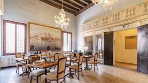 Un comedor amplio con mesas y sillas de madera, una araña y un cuadro grande de un paisaje urbano.