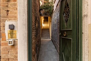 A narrow alleyway leading to a staircase, with a green door on the right and a plaque on the left.