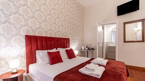Une chambre d’hôtel avec un grand lit, une tête de lit rouge, une table de chevet avec une lampe et un miroir au mur.