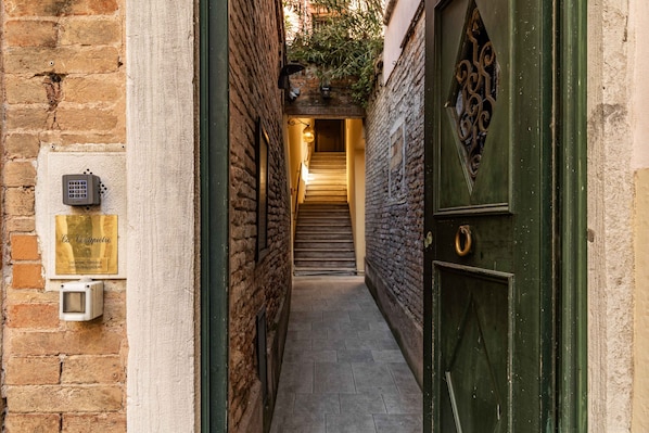 Un estrecho callejón que conduce a una escalera, con una puerta verde a la derecha y una placa a la izquierda.