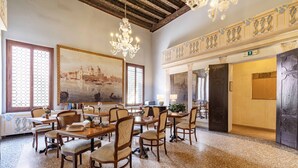 Une salle à manger spacieuse, avec des tables et des chaises en bois, un lustre et un grand tableau représentant un paysage urbain.