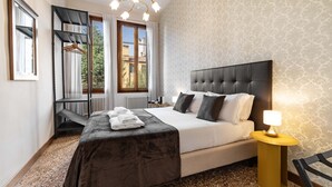Habitación de hotel con cama, mesita de noche con lámpara, ventana con cortinas, radiador y perchero.