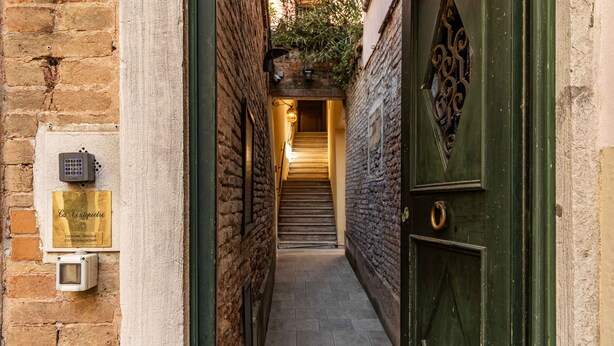 Un étroit passage menant à un escalier, avec une porte verte sur la droite et une plaque commémorative sur la gauche.