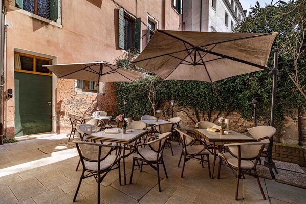 Une terrasse extérieure avec des tables et des chaises, des parasols, et un bâtiment en arrière-plan.