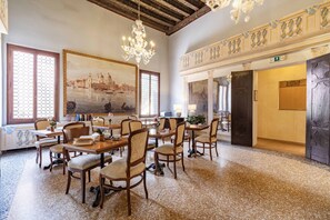 Un comedor amplio con mesas y sillas de madera, una araña y un cuadro grande de un paisaje urbano.