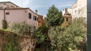 Une ruelle étroite bordée de bâtiments des deux côtés, avec un arbre au centre et un petit espace extérieur aménagé avec des tables et des chaises.