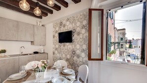 A dining area with a table set for four, a kitchen with a modern design, and a city view through a window.