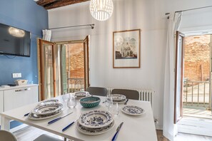 Un coin repas avec une table dressée pour quatre personnes, un téléviseur fixé au mur et une grande fenêtre donnant sur un mur de briques.