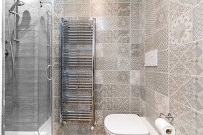 Een badkamer met een douchecabine van glas, een handdoekrek, een toilet en betegelde vloeren.