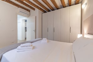Een slaapkamer met een bed, witte lakens, een houten plafond en een kledingkast.