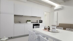 A modern kitchen with white cabinetry, a dining table with white chairs, a microwave, and a small potted plant. - Bellini Design by Wonderful Italy (Venecia)