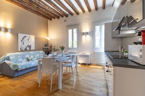 Una cucina moderna con piano cottura integrato, un'area pranzo con tavolo apparecchiato per due e un soggiorno con divano e un quadro.
