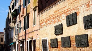A narrow street with old buildings, some with visible wear and others with decorative plaques. - Ca' Forner by Wonderful Italy (Venecia)