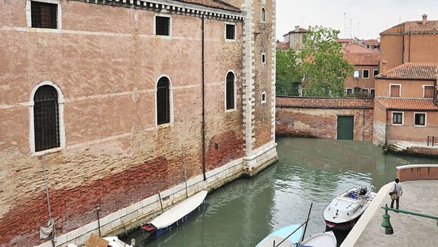 Ein Kanal mit anliegenden Booten, ein historisches Gebäude mit einem Turm und eine Brücke im Hintergrund.