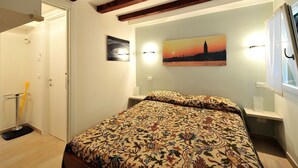 A bedroom with a bed, a painting of a sunset, and a night light. - Creme Caramel Room by Wonderful Italy (Venecia)
