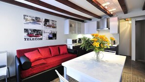 Eine moderne Küche mit weißen Schränken, einer schwarzen Arbeitsplatte und einem roten Sofa mit Kissen. Auf der Arbeitsplatte steht eine Vase mit gelben Blumen.