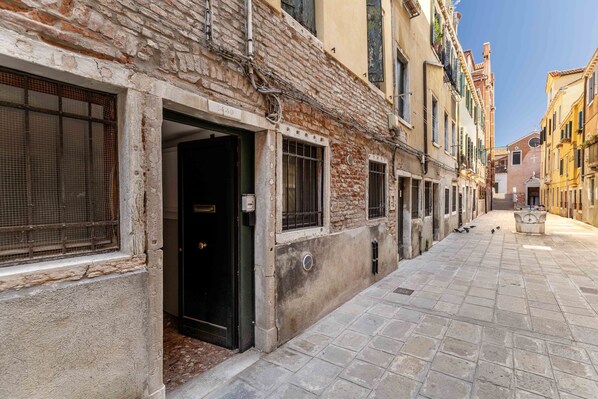 A narrow street with buildings on either side, featuring a mix of brick and plaster facades, some with visible wear and tear.