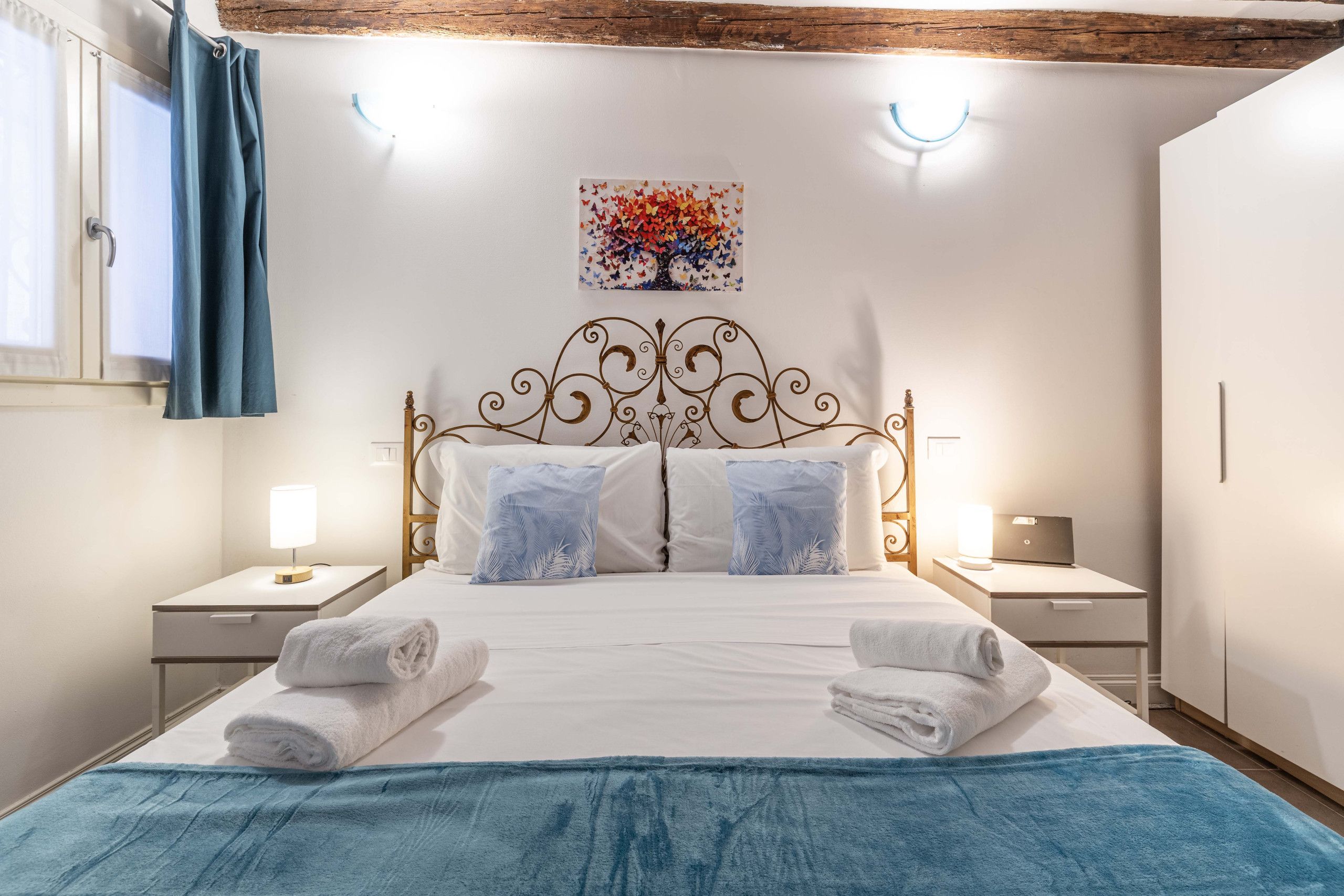 Ein ordentlich bezogenes Bett mit weißen und blauen Handtüchern, einer Wanddekoration und einer Holzbalkendecke.