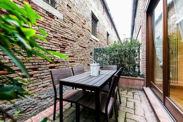 A brick wall with a window, a table with chairs, and a small garden area.