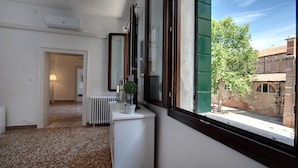 Ein Zimmer mit Heizkörper, einer Topfpflanze und einem Fenster mit Blick auf einen Innenhof und Gebäude.
