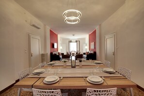 Un comedor con una mesa larga dispuesta para seis personas, rodeada de sillas blancas, con una moderna lámpara de araña colgando.