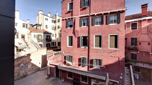 A red building with multiple windows and balconies, a visible staircase, and a narrow street. - Pozzo Roverso by Wonderful Italy (Venecia)