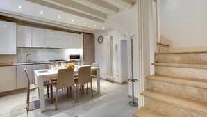 A modern kitchen with white cabinets, a dining table set for four, and a staircase with wooden steps. - Pozzo Roverso by Wonderful Italy (Venecia)