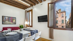 A dining area with a table set for two, a sofa, and a TV mounted on the wall. - Ca' Beccarie 1 by Wonderful Italy (Venecia)