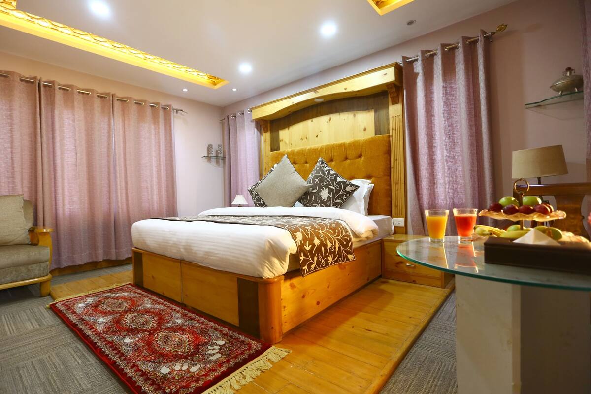 A well-lit bedroom with a wooden bed, a glass table with fruit, and a red patterned rug.