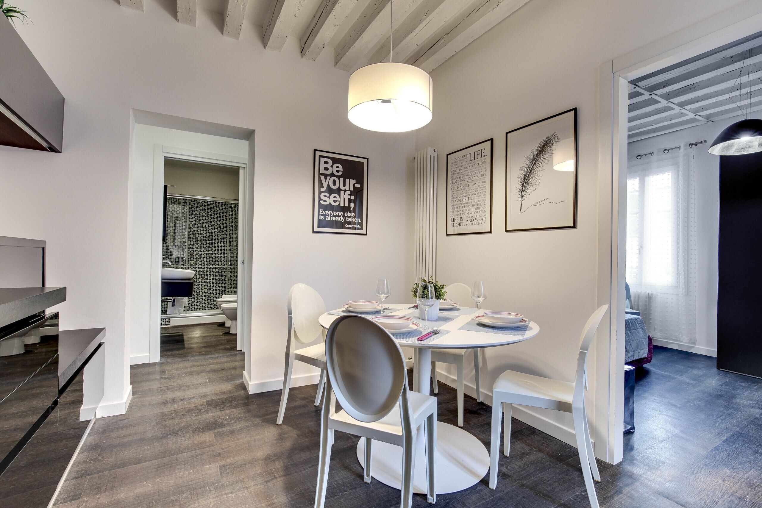 Een moderne eethoek met een ronde tafel voor vier personen, witte stoelen en een plafond met zichtbare balken.