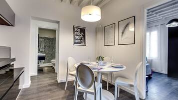 Een moderne eethoek met een ronde tafel voor vier personen, witte stoelen en een plafond met zichtbare balken.