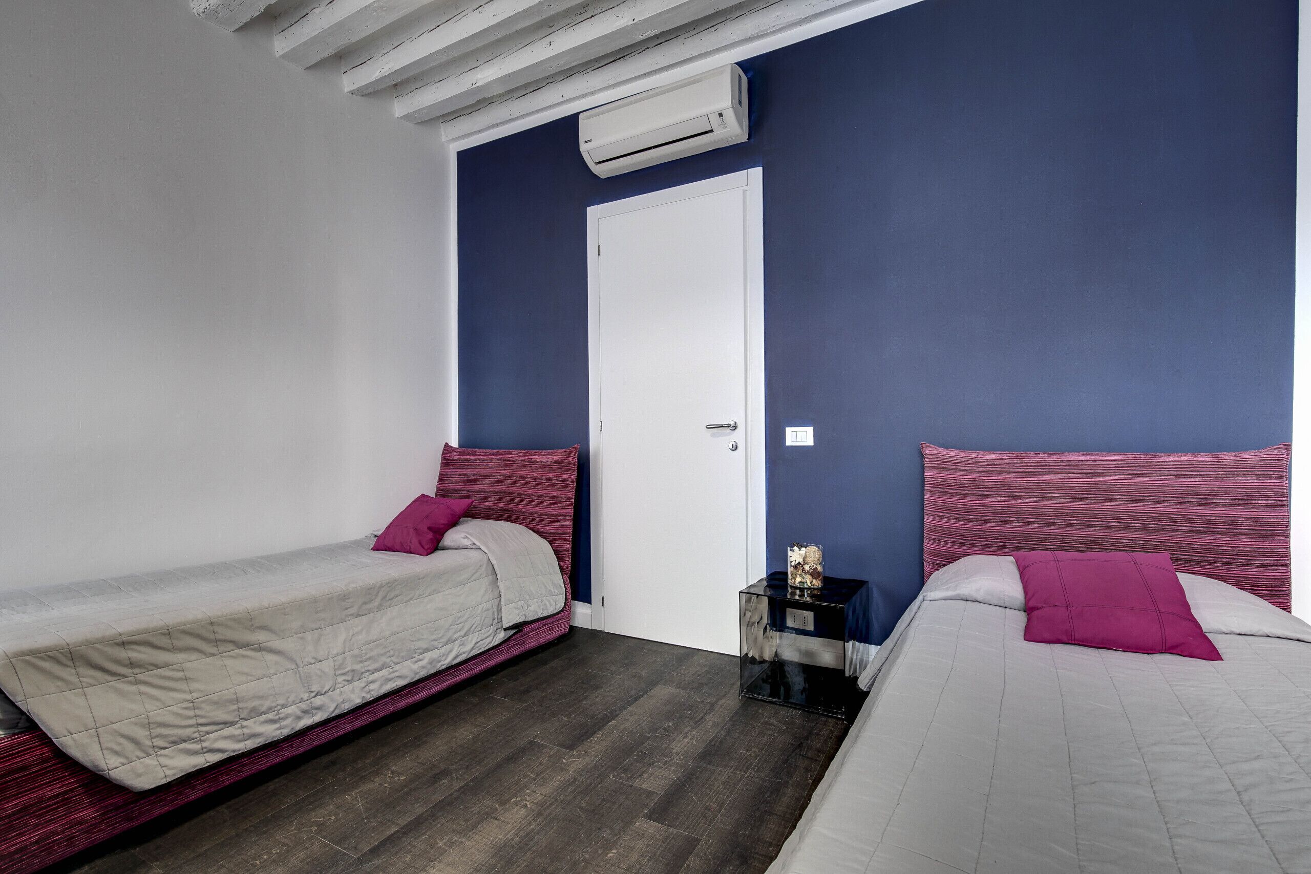 Una camera da letto con due letti, una porta bianca e un condizionatore d'aria.