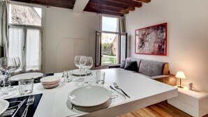 Un espace repas moderne avec une table blanche dressée pour deux personnes, un canapé et une lampe.