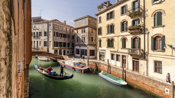Un canal con góndolas y barcos, edificios con balcones, y un puente al fondo.