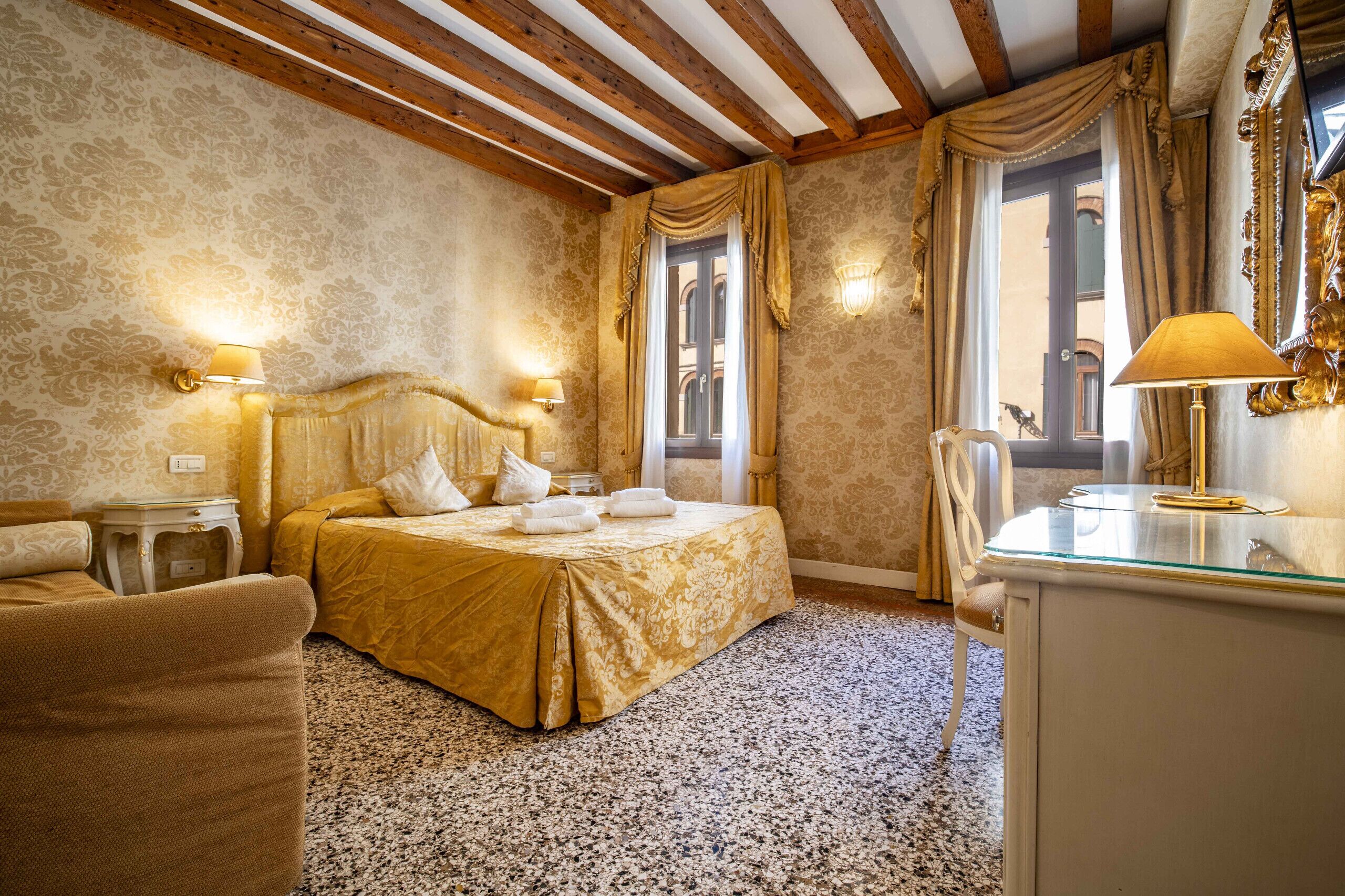 Een hotelkamer met een bed, een bureau en een stoel. Er hangen twee lampen aan de muur.