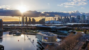 A modern cityscape with a river, a prominent building with a circular design, and a skyline with various high-rise buildings.
