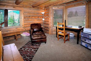 A log cabin interior with a leather chair, a wooden dining table, and a desk with a printer.