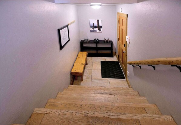 A wooden staircase leading to a room with a bench and a small table, a door, and a framed picture on the wall.