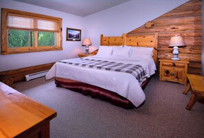 A cozy bedroom with a wooden headboard, a large bed with a checkered bedspread, two bedside lamps, and a window with blinds.