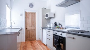 A modern kitchen with white cabinetry, a wooden door, a microwave, a kettle, and a toaster. - Sea Glass - 2 Bedroom Apartment - Manorbier (Tenby)