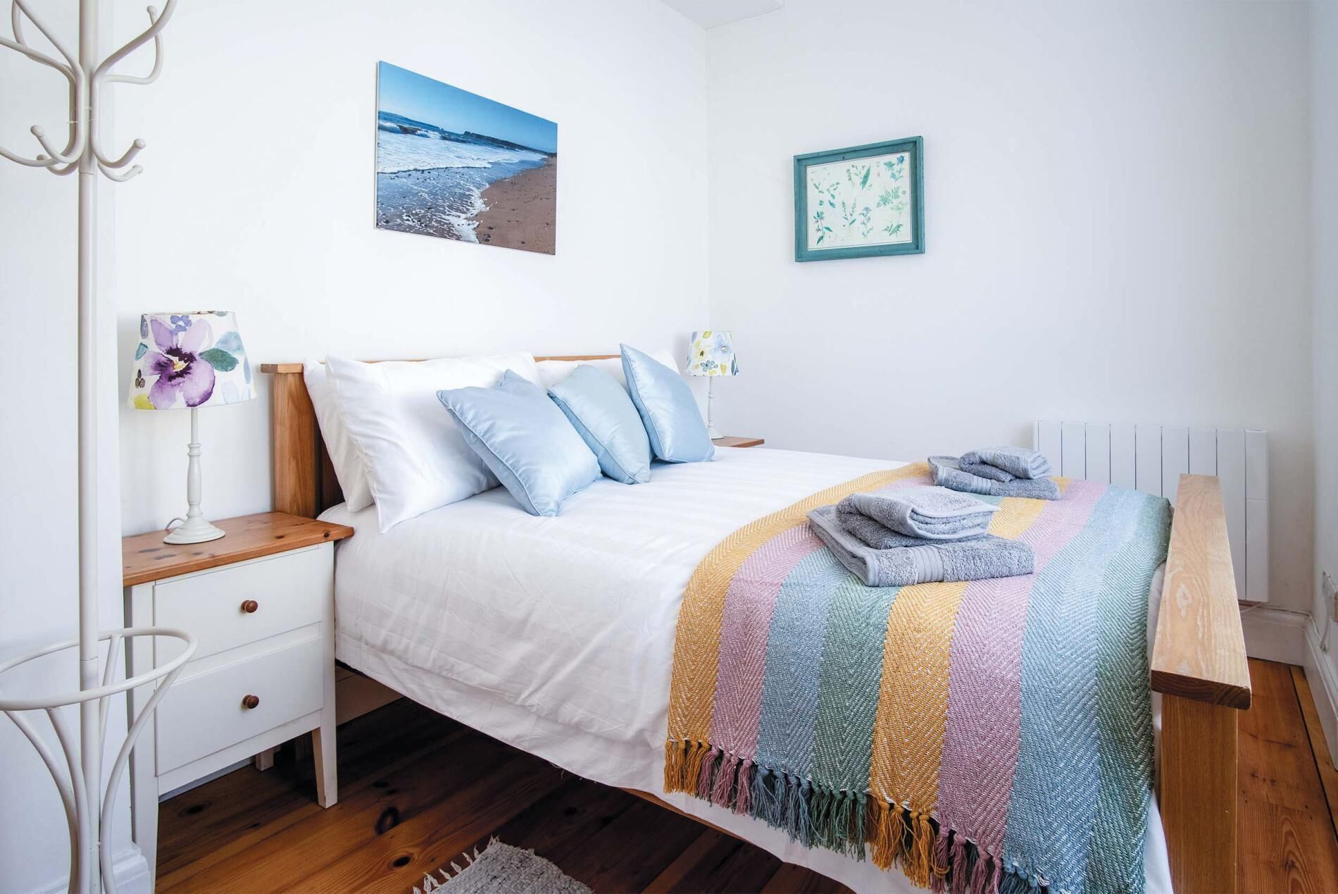 A bedroom with a bed, bedside tables, a lamp, a blanket, and a wall with a picture.