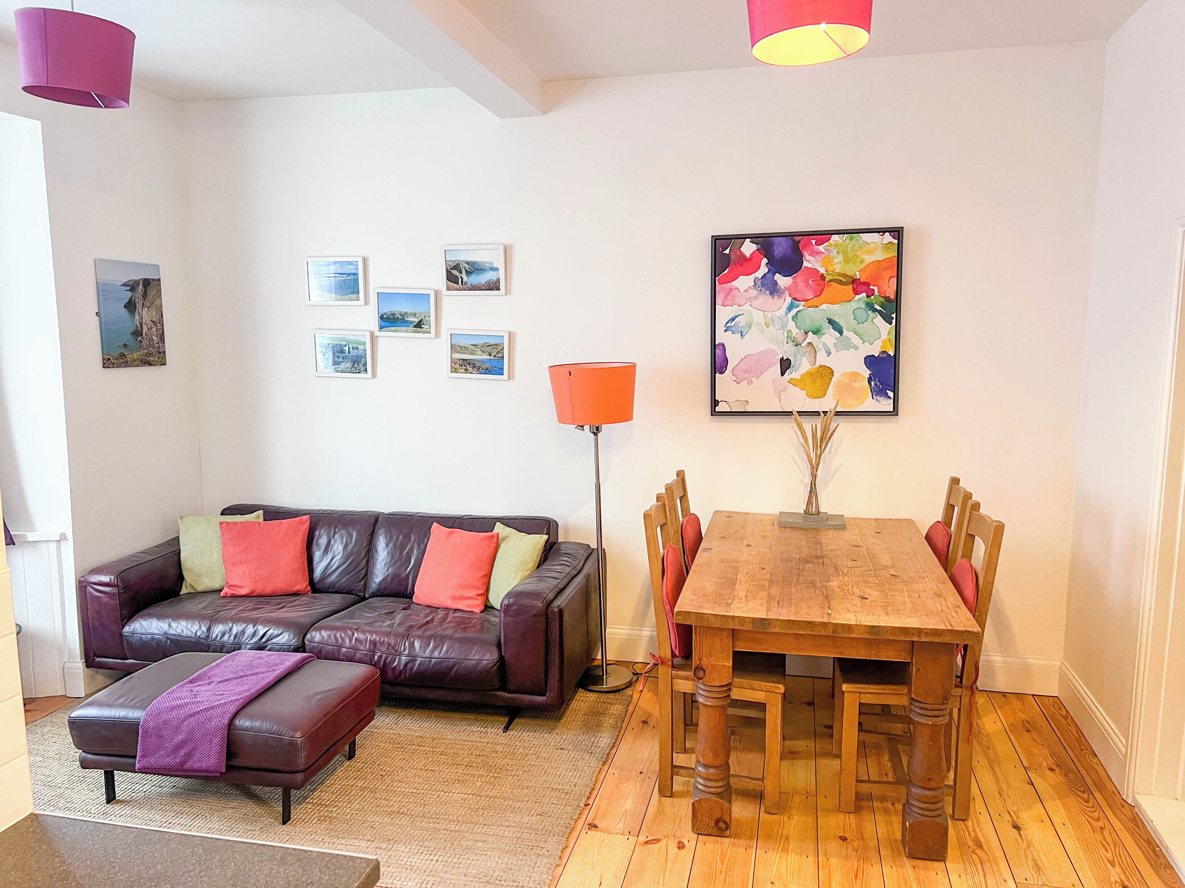 Un soggiorno con un divano in pelle, un tavolo da pranzo in legno e un quadro astratto dai colori vivaci appeso al muro.
