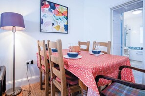 Ein Essbereich mit rotem Tischlein, Holzsesseln und einer modernen Stehlampe.