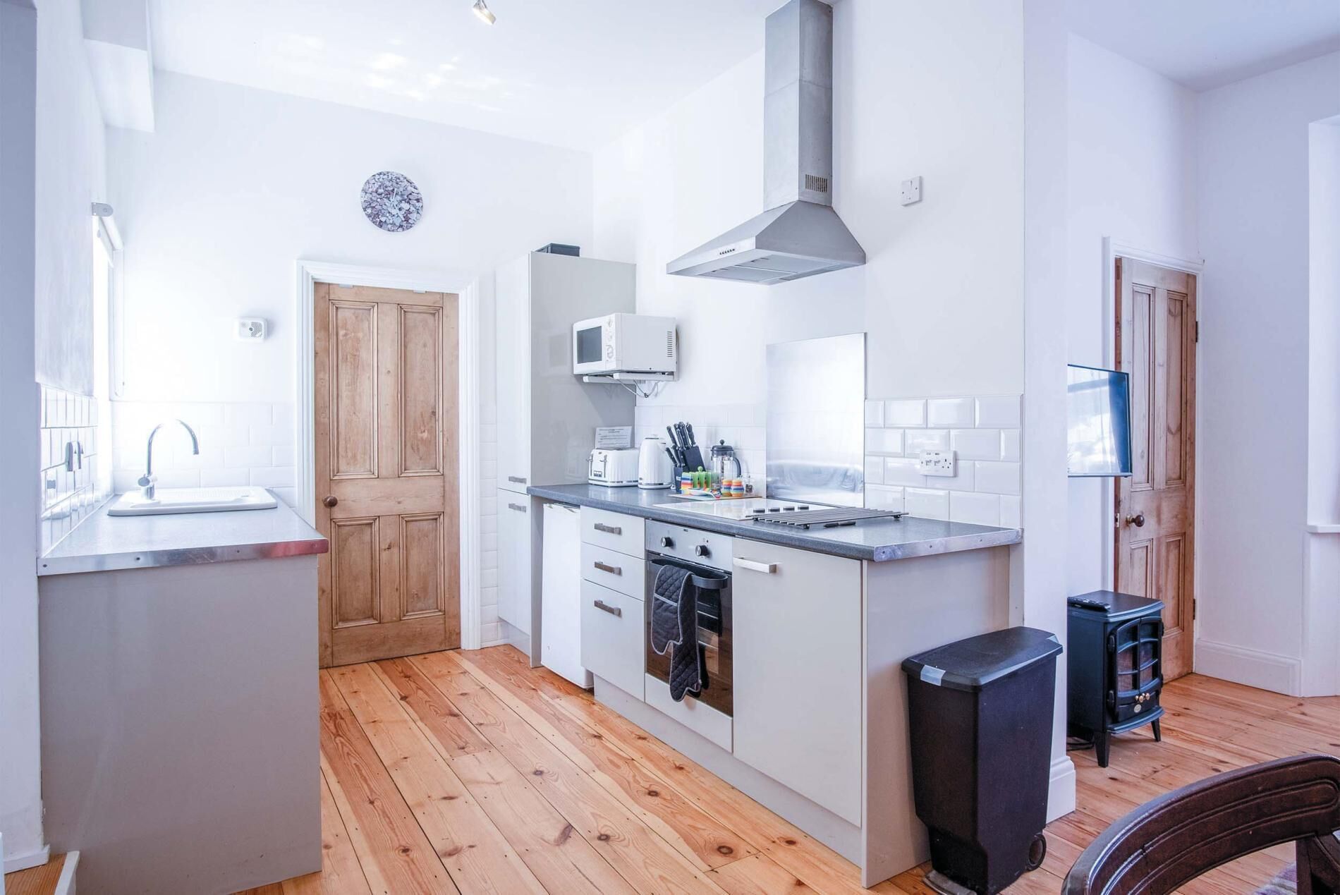 A modern kitchen with wooden flooring, white cabinetry, a built-in oven, and a stainless steel range hood.