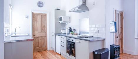 A modern kitchen with wooden flooring, white cabinetry, a built-in oven, and a stainless steel range hood.
