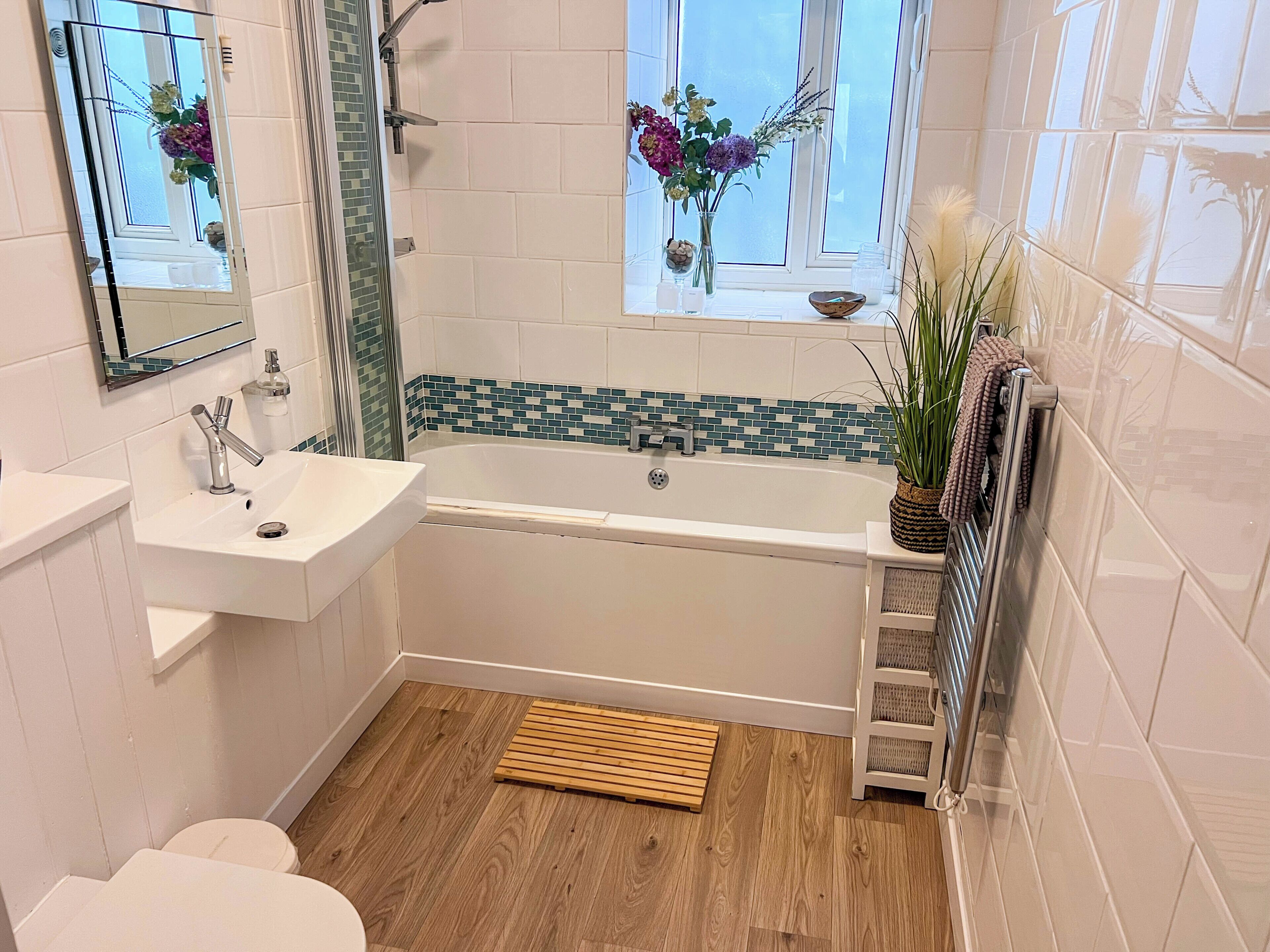 Une salle de bain avec une baignoire, un lavabo, des toilettes et une fenêtre décorée de fleurs.