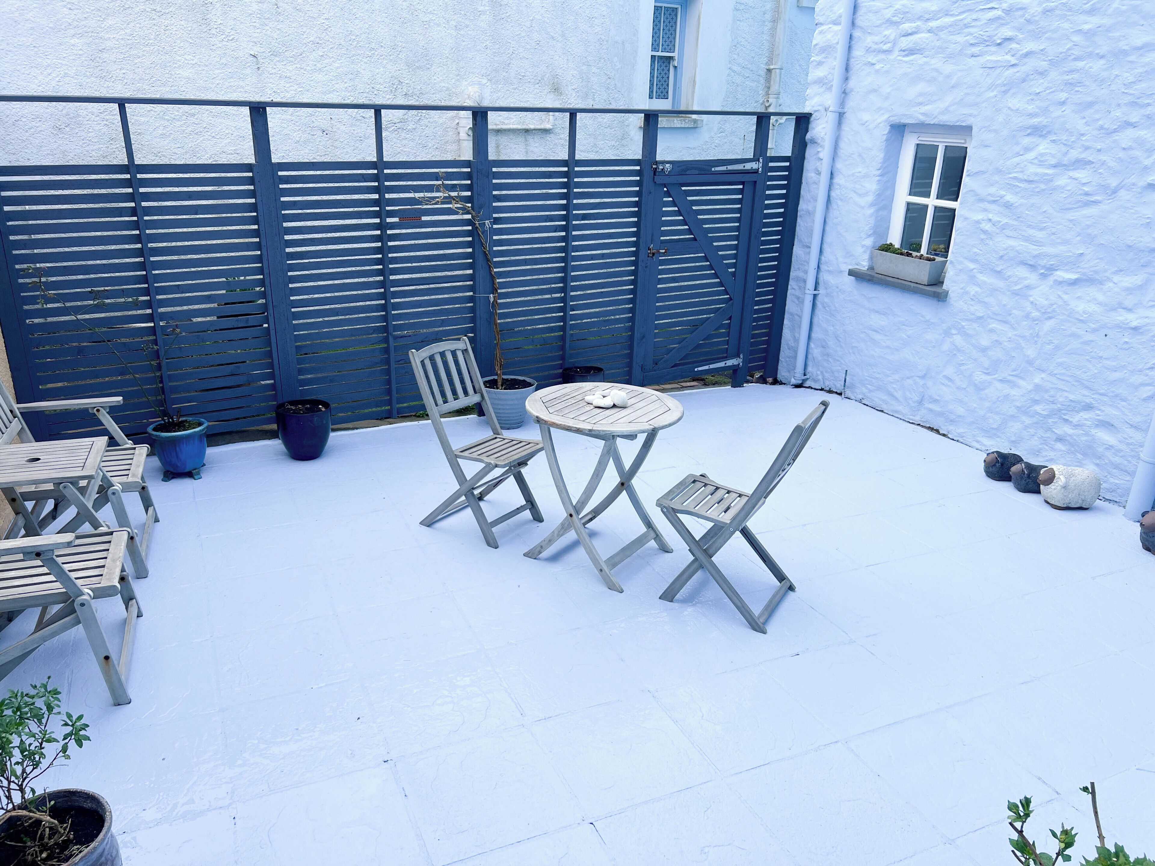 A patio with a table and chairs, a blue fence, and potted plants.